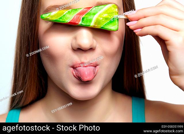 Teenager girl with with lollipop in hands closing eyes and showing tongue. Sweet tooth concept