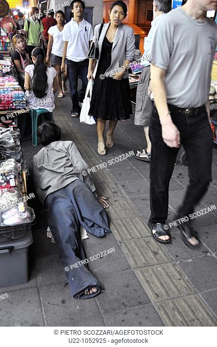 Bangkok (Thailand): beggar laying on the sidewalk in the Nana area, along Sukhumvit Road