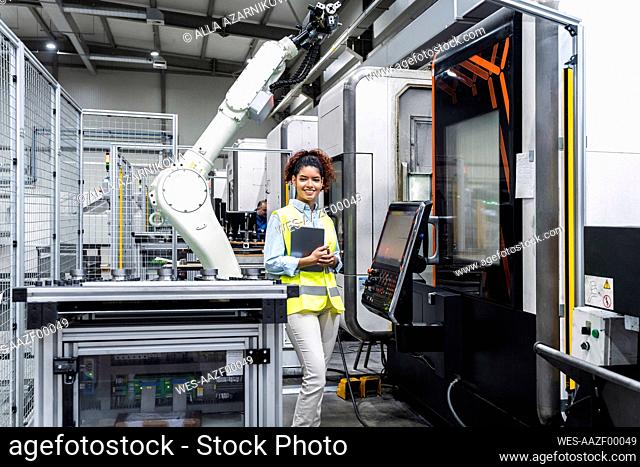 Smiling engineer standing with tablet computer by machine in factory