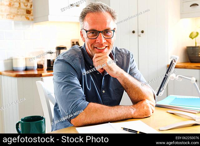Portrait of happy caucasian man sitting at table in kitchen
