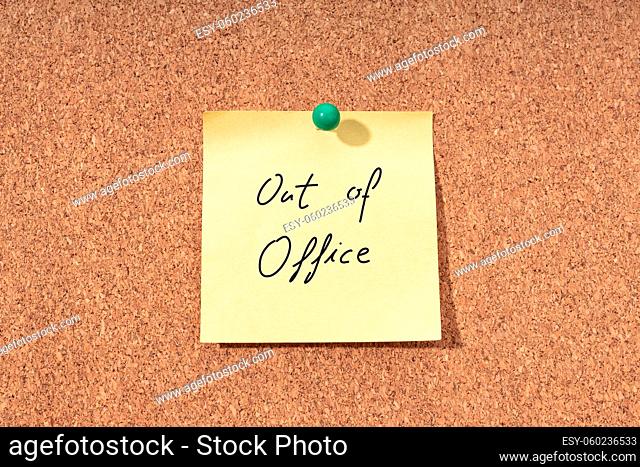 Yellow note with phrase out of office on cork board