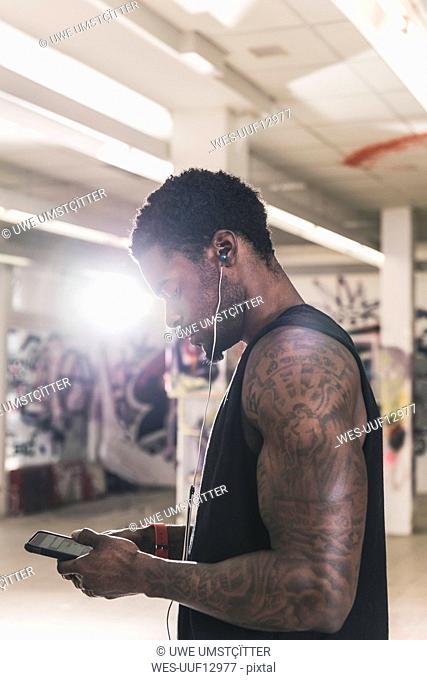 Man with tattoos in cellar with smartphone and earphones