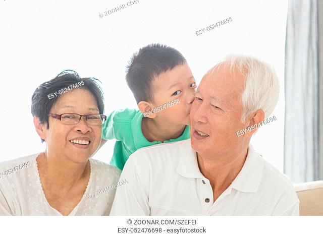 Portrait of happy Asian grandchild kissing grandparents at home, old senior retired people and child indoor lifestyle