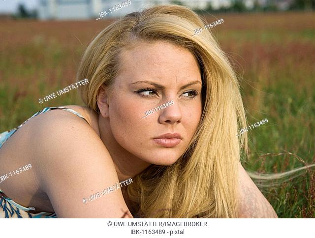 Young blonde woman lying in a meadow, pensive