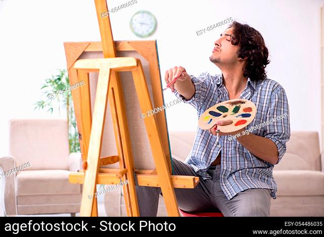 The young handsome man enjoying painting at home