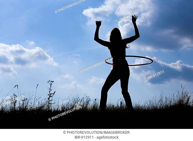Silhouette of a young woman with a hula hoop in front of a cloudy sky