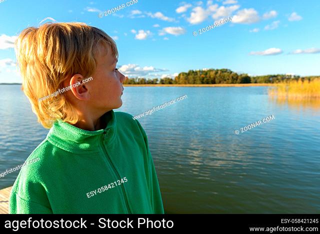Portrait of young handsome boy with blond hair at wooden pier against view of the river