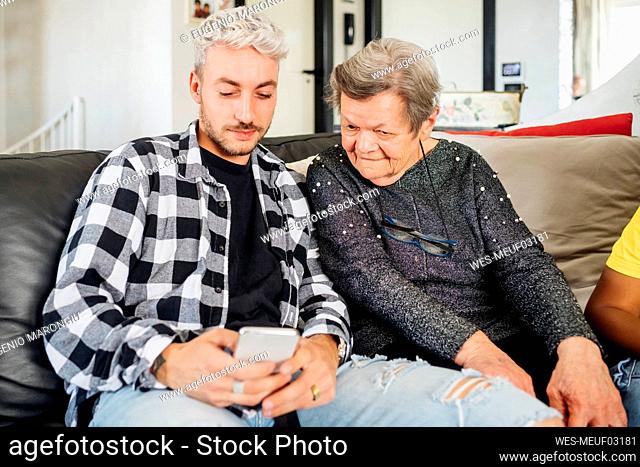 Young man sharing mobile phone with grandmother at home