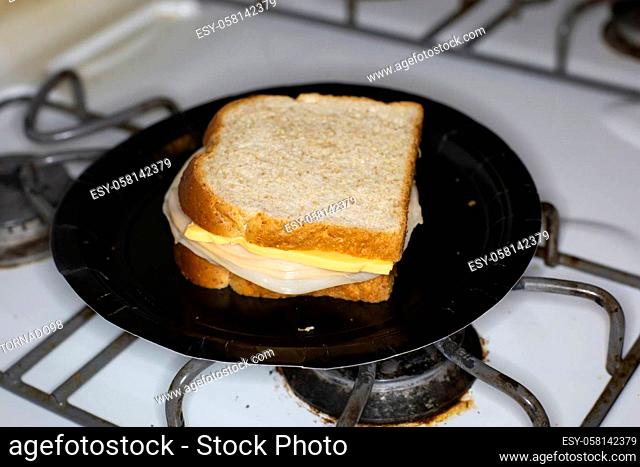 Sliced chicken and cheese sandwich slathered in mustard, on a black paper plate on the stove