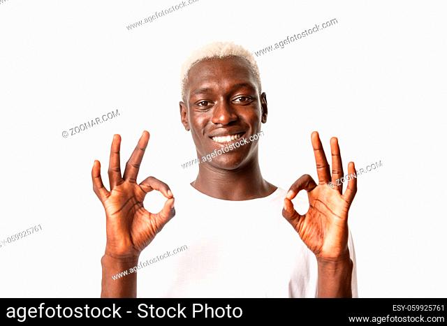 Close-up of satisfied attractive african-american blond guy showing okay gesture and smiling, like and approve, standing over white background