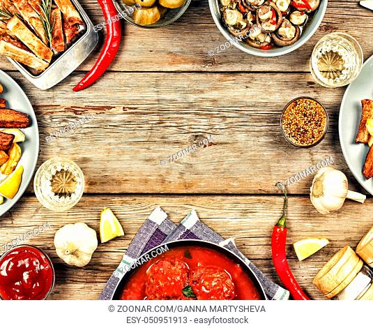 Dining table with a variety of meals and snacks. Meatballs, baked potato wedges, meat, mushrooms, ketchup. Wooden background, top view. Rustic style