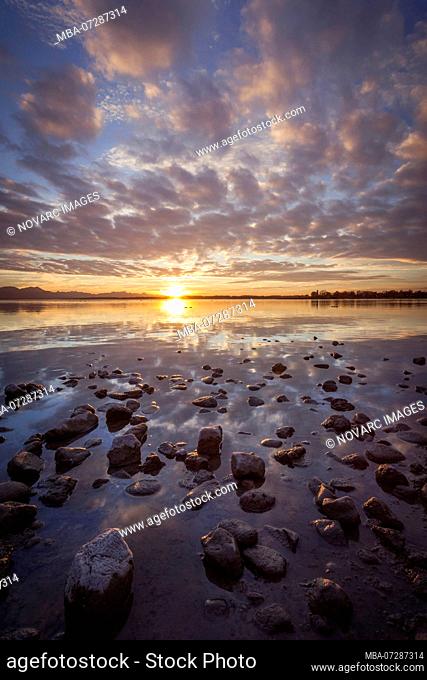 Cloud reflection in the Chiemsee beach with stones and colorful clouds, Seebruck, Bavaria, Germany