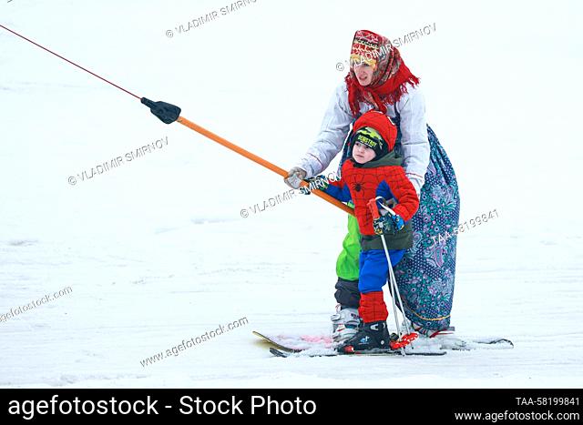 RUSSIA, IVANOVO REGION - APRIL 2, 2023: Dressed up snowboarder and skier use a surface lift during the 2023 edition of Easy-Freezy Festival at Milovka ski...