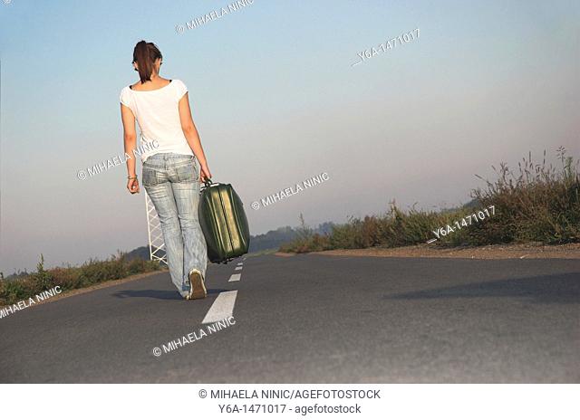 Young woman carrying suitcases on road, rear view