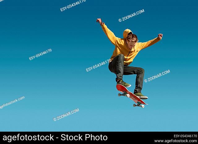 A teenager skateboarder does an ollie trick in a skatepark on the outskirts of the city On a background of blue sky gradient