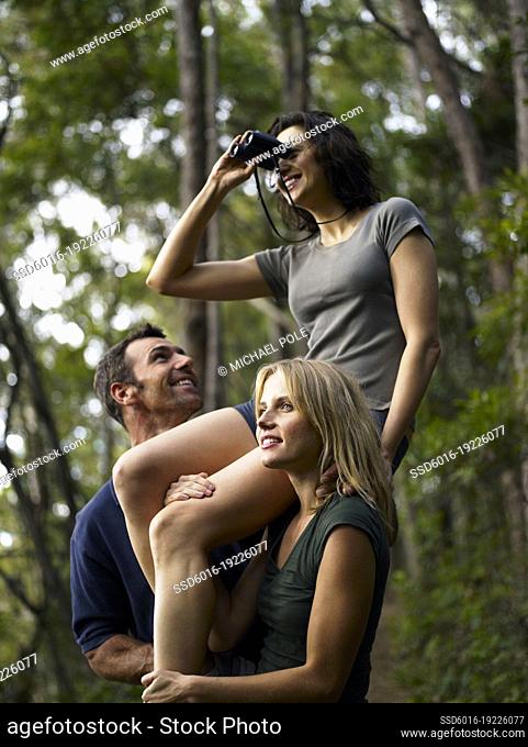 Woman sitting on friends shoulders looking through binoculars in Australian bush
