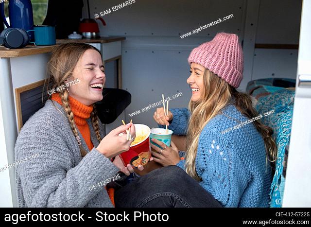 Happy young women friends eating instant noodles in camper van