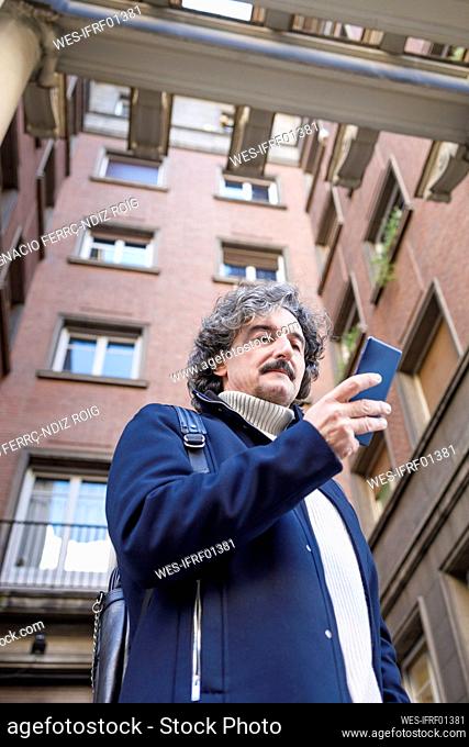 Man text messaging on smart phone in front of building