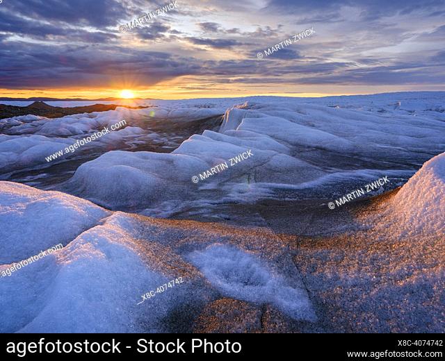 Midnight sun on the ice sheet. The brown sediment on the ice is created by the rapid melting of the ice. Landscape of the Greenland ice sheet near Kangerlussuaq