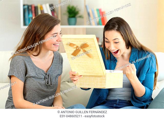 Excited woman receiving a gift from a friend sitting on a couch in the living room at home