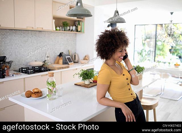 Smiling young woman talking on smart phone in kitchen