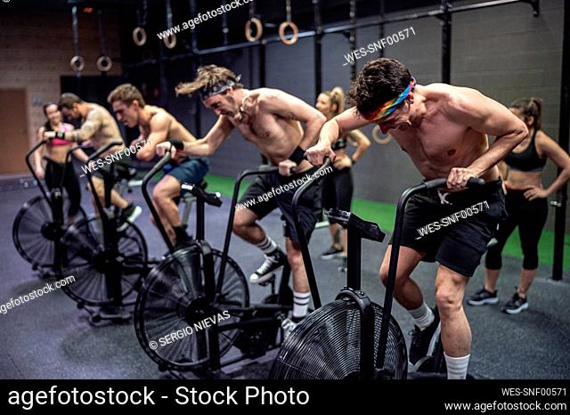 Athletes cycling on exercise bike with women standing in background at gym