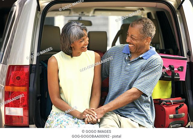 Middle-aged African couple sitting in trunk of their SUV