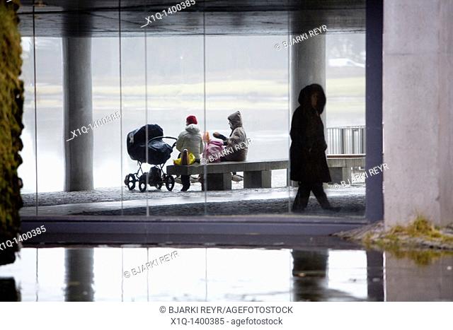 A family enjoying a picnic outside during a rainy, foggy day  Person walking by  Reykjavik City Hall, downtown Reykjavik, Iceland