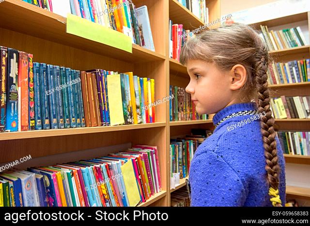 The girl chooses books in the library