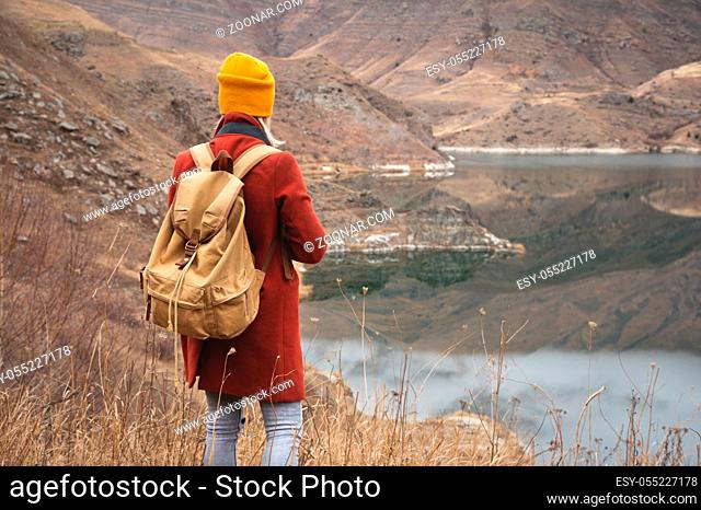 A portrait from the back of a girl traveler on the background of a lake in the mountains in autumn or early spring. Travel concept