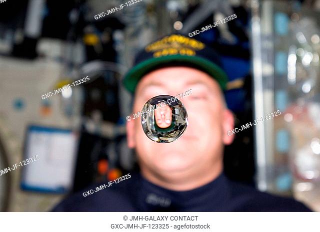 NASA astronaut Alan Poindexter, STS-131 commander, watches a water bubble float freely between him and the camera, showing his image refracted