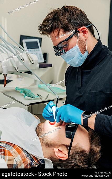 Dentist examining patient's teeth with equipment in clinic