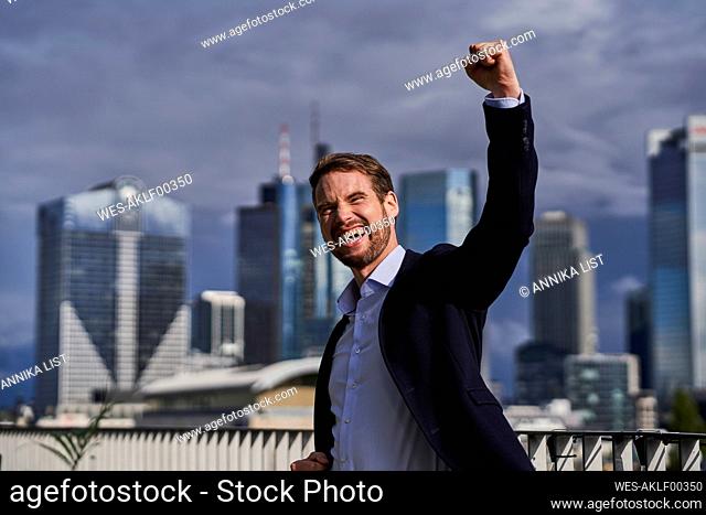 Cheerful businessman with hand raised celebrating at building terrace