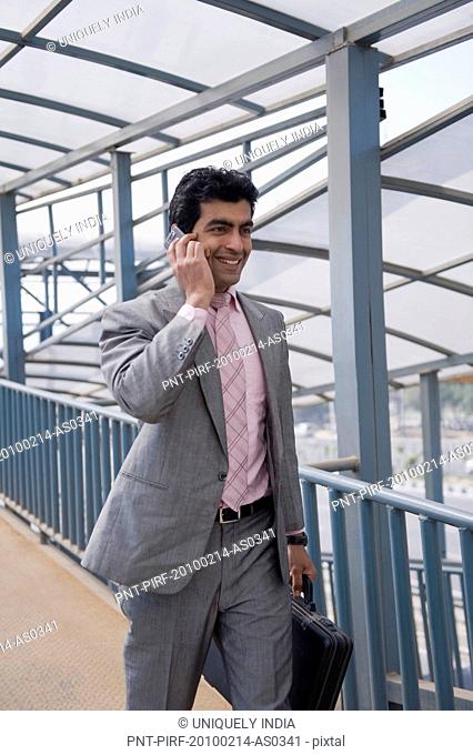 Businessman talking on a mobile phone on a footbridge, Gurgaon, Haryana, India