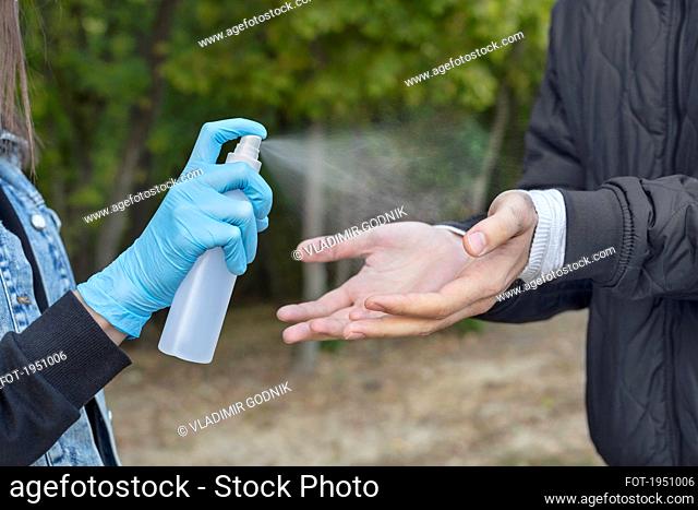 Close up woman in protective gloves spraying boyfriend with hand sanitizer