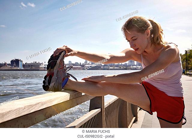 Young woman exercising outdoors, stretching, beside river, New York City, USA