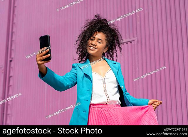 Smiling young woman holding skirt while taking selfie on sunny day