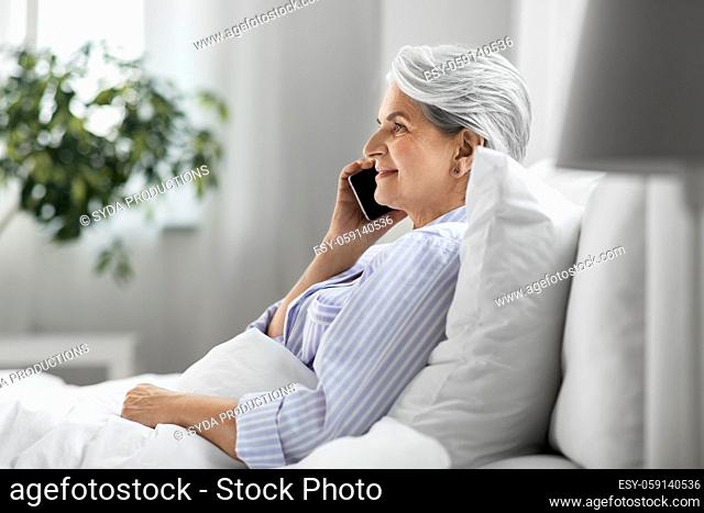 senior woman calling on smartphone in bed at home
