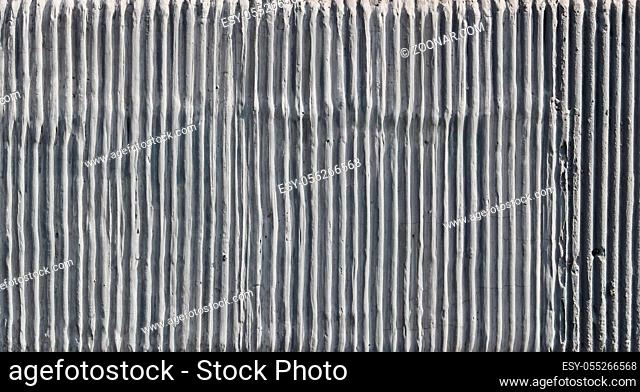 The wall of the old building is decorated with a texture of vertical cement uneven wavy strips. Sunny day outdoor shot