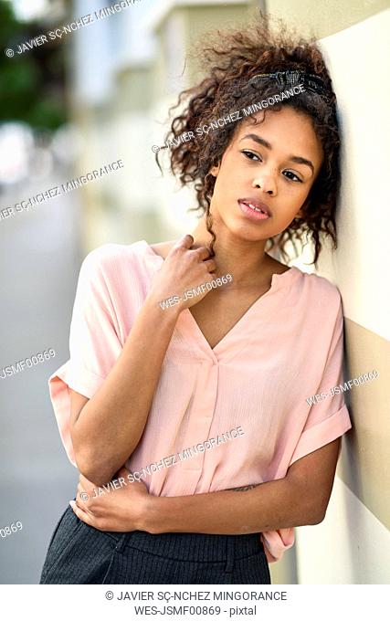 Serious young woman leaning against a wall looking around