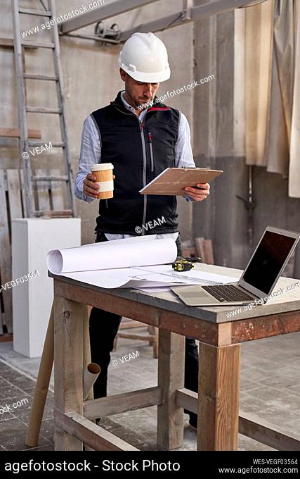 Male architect holding coffee while analyzing plan in building