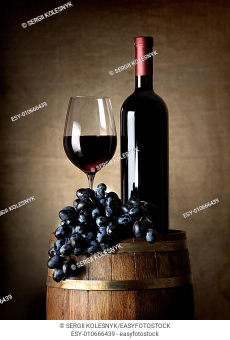 Bottle of red wine, wine glass, grapes and wooden barrel