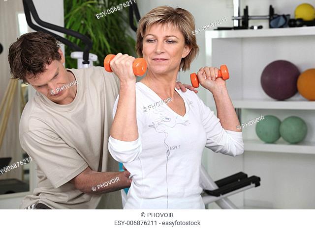 Mature woman working out with dumbbells and a personal trainer