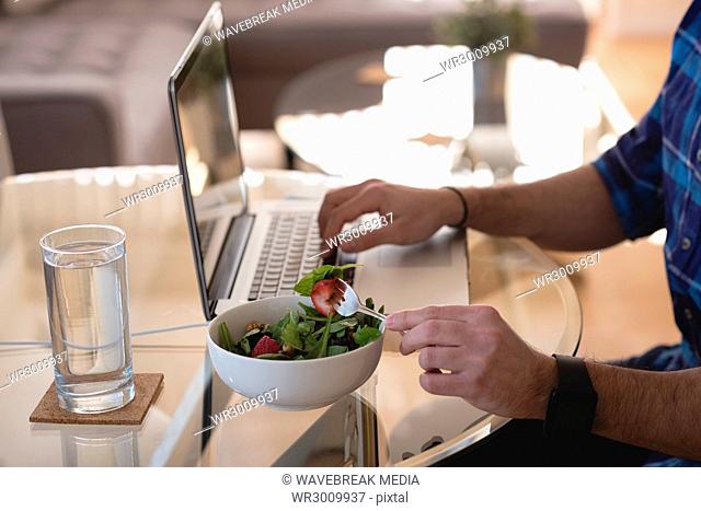 Man using laptop while having breakfast in living room