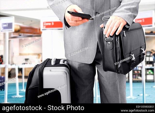 Traveling businessman with his luggage using phone at the airport