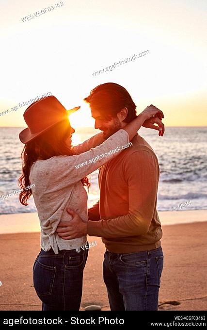 Young couple dancing while standing on beach during sunrise