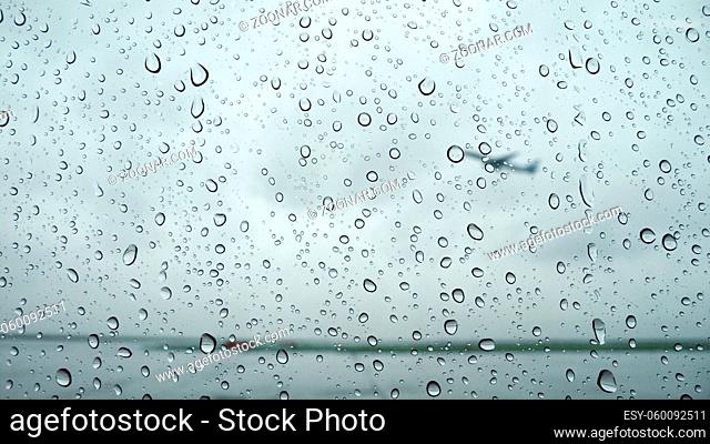 raindrops background on airport window with flying plane behind