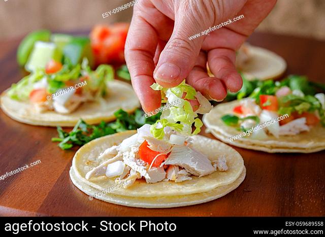 A close up studio photo of putting shredded lettuce on a street taco