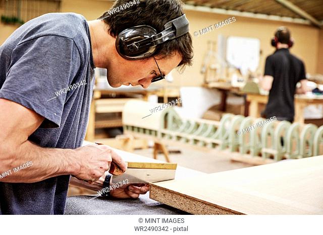 A furniture workshop making bespoke contemporary furniture pieces using traditional skills in modern design. A man using a small handsaw to trim wood