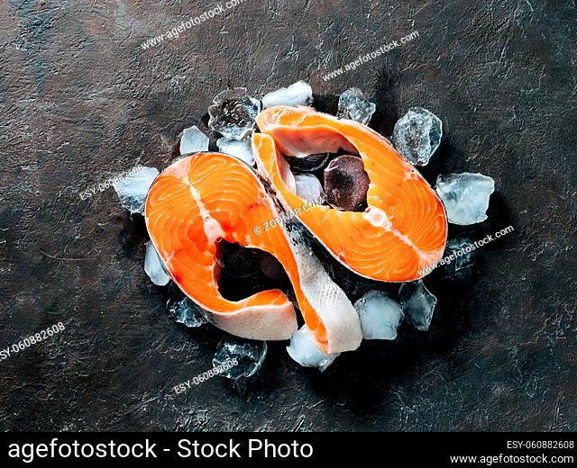 Two raw wild salmon steaks on ice over black textured background. Salmon steaks top view or flat lay